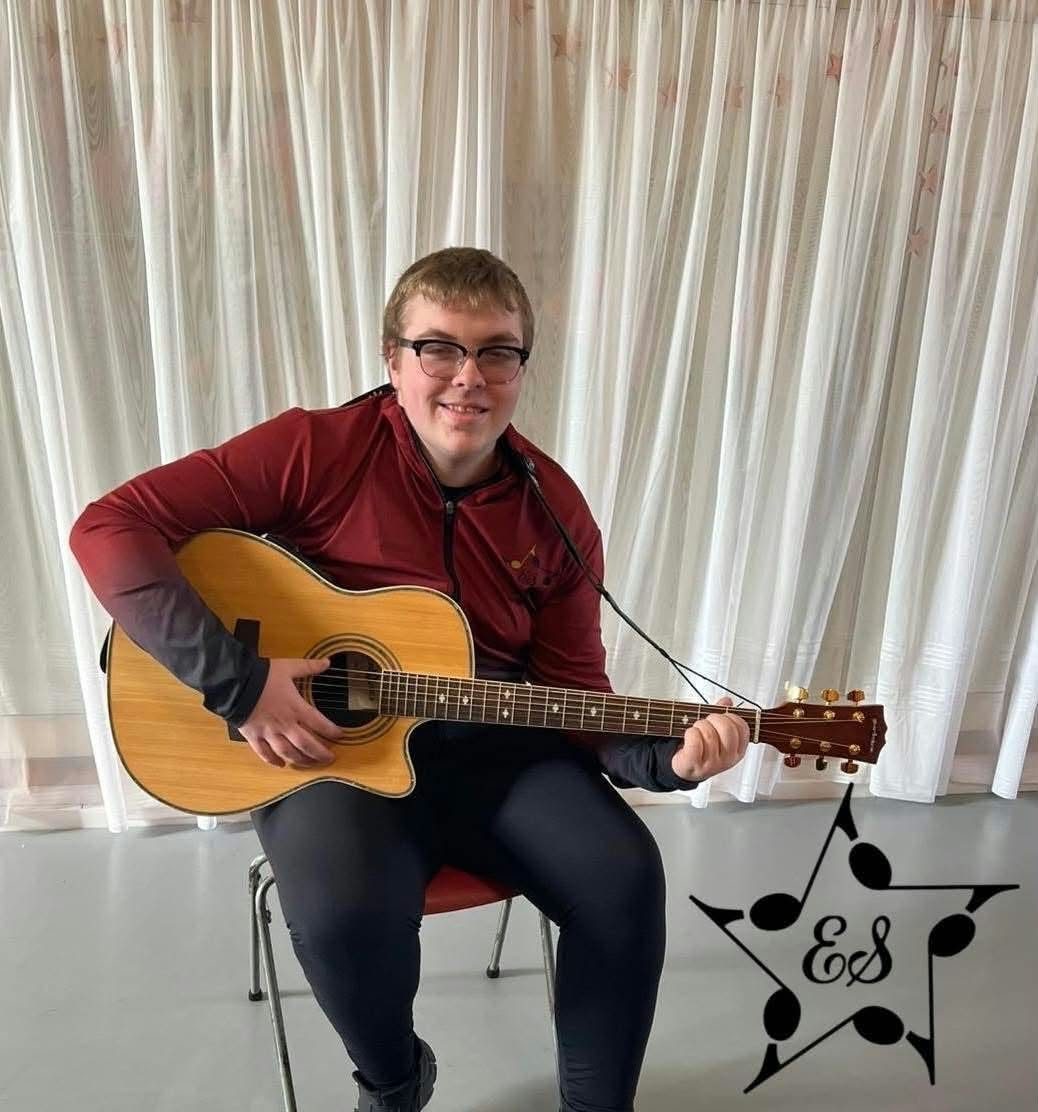 A teenage student smiling while playing an acoustic guitar in the ESSOPA studio